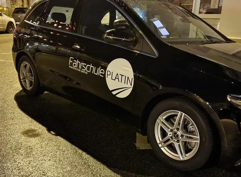Schwarze Mercedes B-Klasse mit dem Schriftzug Fahrschule Platin am Abend